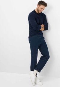 Maglione blu navy e pantaloni blu navy abbinati con risvolti. Sneakers bianche con suole visibili. Texture liscia, design casual.