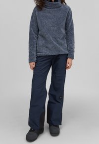 Polarowy golf w ciemnym szarym kolorze, zestawiony z granatowymi wodoodpornymi spodniami z czarnymi akcentami oraz teksturowanymi butami.