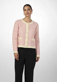 Cardigan à manches courtes en crème et rose, présentant un motif à carreaux texturé, des poignets côtelés et un front à six boutons avec deux poches plaquées.