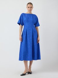 Blau strukturiertes Midikleid mit Bootsausschnitt und kurzen Ärmeln. Verfügt über einen plissierten Rock und glatte schwarze Mules. Einfaches und elegantes Design.