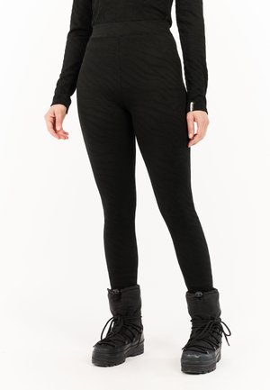 Schwarze Leggings mit einem strukturierten Zickzackmuster, hohem Bund und enger Passform. Kombiniert mit knielangen schwarzen Winterstiefeln.