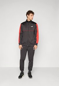 Tracksuit atlético preto com casaco com fecho de correr e detalhes vermelhos e calças a condizer. Feito de material liso e leve.