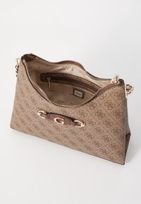 Borsa a spalla marrone con motivo monogramma, hardware dorato e tracolla di un marrone scuro a contrasto. Parte superiore aperta che rivela un interno foderato con una tasca con cerniera.