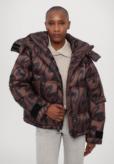 Brown puffer jacket with black swirl pattern, featuring a hood, zip closure, and ribbed cuffs. Layered over a light beige knit top.