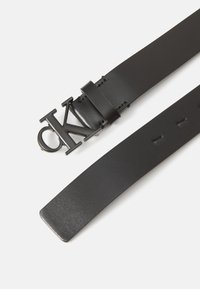 Svart läderbälte med matt yta, försedd med en stor svart metallspänne med "CK"-logotyp och flera hål för justering.