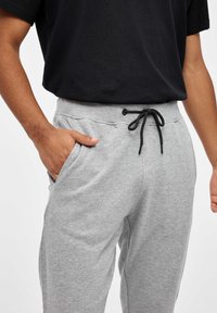 Pantalones de chándal de algodón gris con cintura elástica, cordón negro y bolsillos laterales. Textura suave, ajuste relajado.