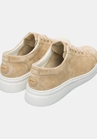 Beige mokkasinikenkiä pyöreällä varvalla, valkoisella kumipohjalla ja sävykkäällä ompeleella. Huomattava tanssiaineksen korostus kantapäässä. Nauhatoiminto.