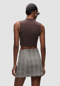 Bruine cropped tanktop van ribstof, gecombineerd met een bedrukte mini rok met een zwart-wit visgraatpatroon.