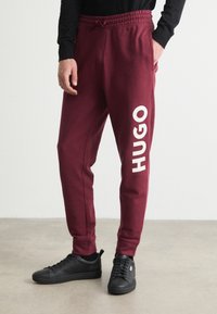 Burgunderfarbene Sweatpants mit einem weißen "HUGO"-Logo an der Seite. Aus weichem Material gefertigt, mit elastischem Bund und seitlichen Taschen.