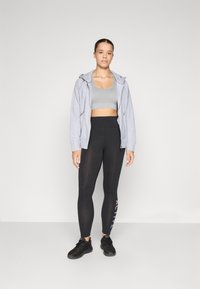 Grå hettegenser med glidelås, lys grå sports-BH, svarte høytliv leggings med "ACTIVE" tekst i rosa. Svarte treningssko. Enkel, tettsittende design.