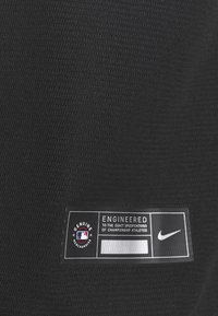 Tissu athlétique noir avec surface texturée. Présente une patch logo qui indique "Marchandise Authentique" et "Conçu selon des spécifications exactes."