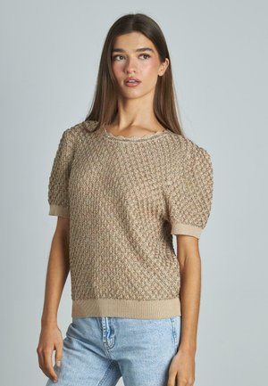 Maglione lavorato a maglia beige con motivo testurizzato, maniche a puff corte e polsini a costine. Collo a scallop e vestibilità morbida. Abbinato a jeans blu chiaro.