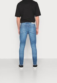 Světle modré džíny s úzkým střihem, mají zadní kapsy a jsou doplněny černobílými teniskami. Triko je černé, krátký rukáv.