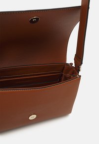 Brązowa skórzana torebka o teksturowanym wykończeniu, wyposażona w złote zapięcie na zatrzask, dwie przegrody i regulowany pasek. Wnętrze podszyte materiałem.