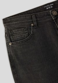 Jeans in denim nero con taglio dritto, caratterizzati da una tasca frontale con dettagli di cucitura e un bottone in metallo sulla vita. Etichetta della taglia visibile.