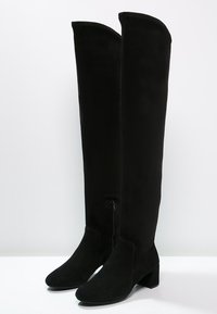 Botas negras por encima de la rodilla, hechas de suave ante, con cremallera lateral, tacón cuadrado y textura lisa sin patrones visibles.