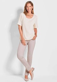 Cremefarbenes, strukturiertes Kurzarmoberteil kombiniert mit hellbeigen, schmal geschnittenen Hosen und passenden Slingback-Schuhen, vor einem neutralen Hintergrund.