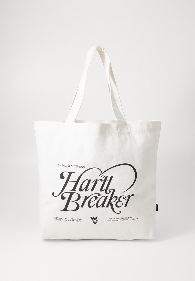 Canvasväska i krämfärg med långa handtag; pryder texten "Hartt Breaker" i fet svart stil och enkla detaljer.