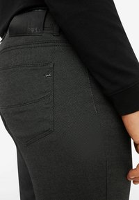 Zwarte denim jeans met een gestructureerde afwerking, voorzien van een rechthoekige achterzak en een leren taillebandlabel met de merknaam.