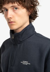 Navy zip-up collar sweatshirt made from soft fabric, featuring a small white logo on the chest and visible stitching details.