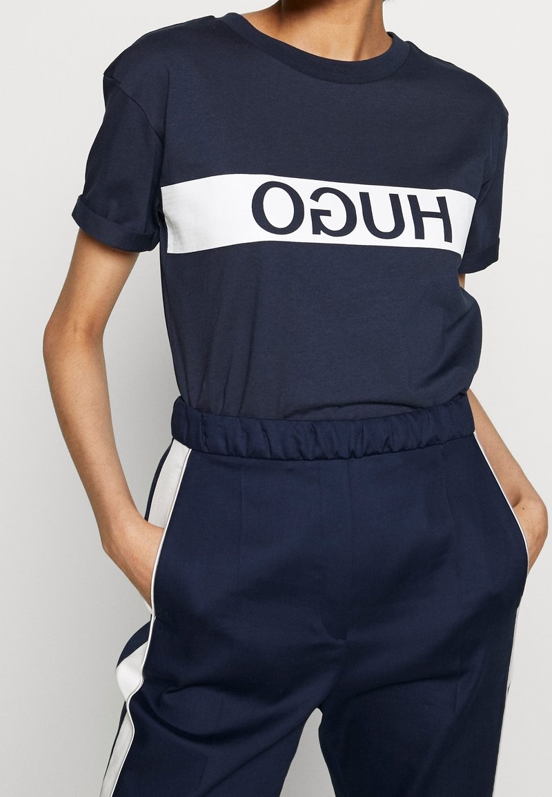 Marineblå bomulds T-shirt med rulleærmer, der har et hvidt vandret bånd med fedt sort "HUGO" bogstaver tværs over brystet.