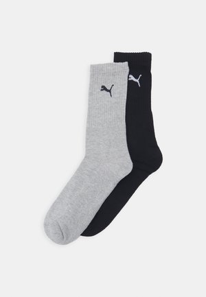 Deux paires de chaussettes à côtes de type crew : une grise claire et une noire, chacune arborant un petit logo Puma blanc sur la partie supérieure.