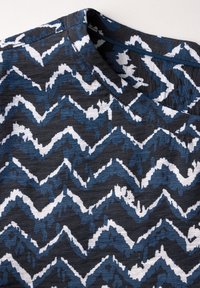 Tessuto a zigzag navy, nero e bianco. Texture morbida con un leggero lucido, dettaglio del colletto rotondo visibile.
