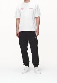 Hvid bomulds T-shirt med rødt "PEGADOR" logo og emblem, parret med sorte sweatpants med hvid "PEGADOR" tekst og elastiske manchetter. Hvide sneakers.