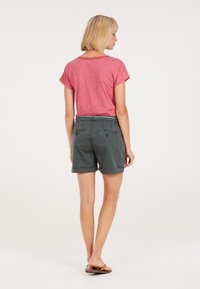 Rood shirt met korte mouwen, gecombineerd met donkergrijze shorts met achterzakken en opgerolde zomen. Model draagt bruine sandaaltjes.