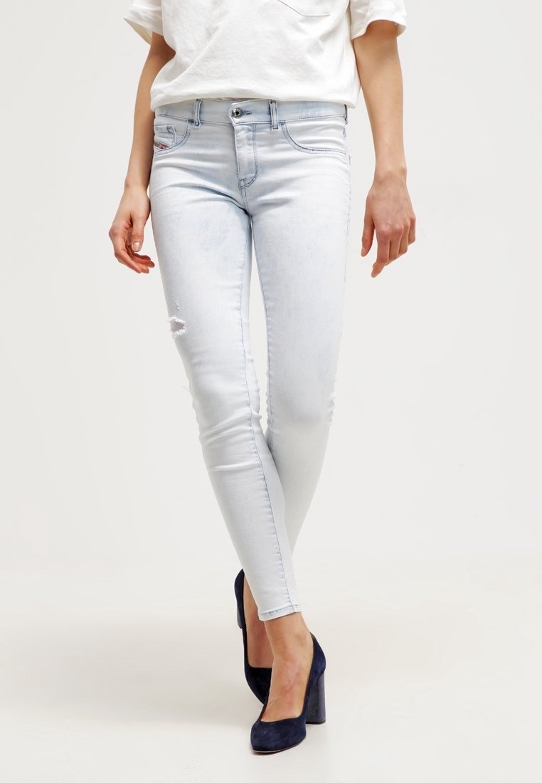 Žena v světle modrých skinny džínách s mírným popraskaním a námořnicky modrých lodičkách, stojící s překříženýma nohama.