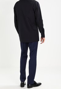 Camicia nera a maniche lunghe con orlo dritto, abbinata a pantaloni blu navy. Caratterizzata da un tessuto morbido, vestibilità su misura e scarpe nere lucide.