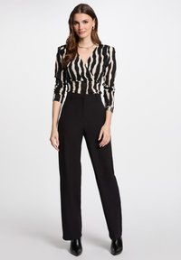 Zwart en beige gestreepte blouse met een diepe V-hals en lange mouwen, gecombineerd met hoge zwarte broeken en elegante zwarte hakken.