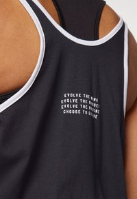 Svart linne med vit kant och motiverande text på baksidan. Tyget är slätt, och designen har breda armhålare för rörlighet.