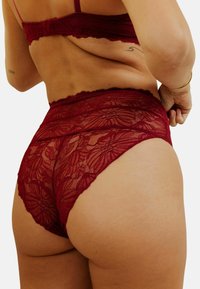 Lingerie en dentelle bordeaux, avec des motifs floraux, une taille haute et un tissu doux et transparent pour une texture délicate.