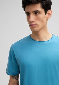 T-shirt à manches courtes, col rond en coton bleu vif. Texture lisse avec des détails de couture au niveau de l'encolure et des manches, sans motifs.