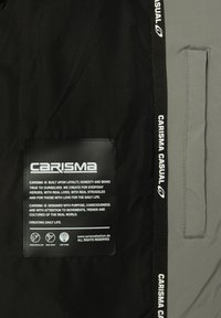 Tessuto nero e grigio con un'etichetta rettangolare nera che presenta del testo bianco. La striscia laterale ha "CARISMA CASUAL" in lettere bianche. Superficie testurizzata.