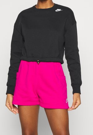 Person wearing black long-sleeve cropped Nike sweatshirt and bright pink Nike shorts with pockets on a neutral background.