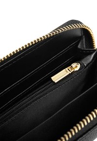 Interno di un portafoglio in pelle nera con zip dorata, dotato di slot per carte e finitura testurizzata. Fodera in tessuto liscio e chiusura con zip sicura.