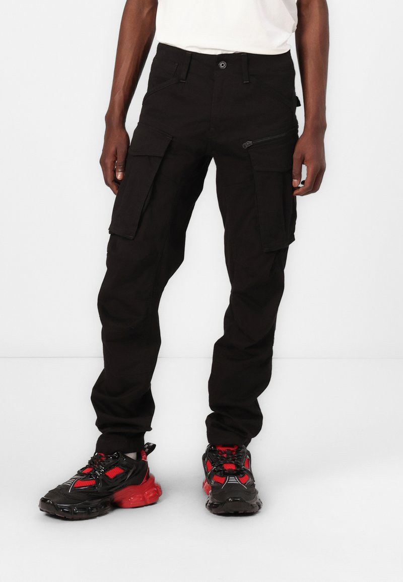 Svarta cargobyxor med flera fickor, en zip-ficka på sidan och en åtsittande design. Bärs med svarta och röda sneakers.