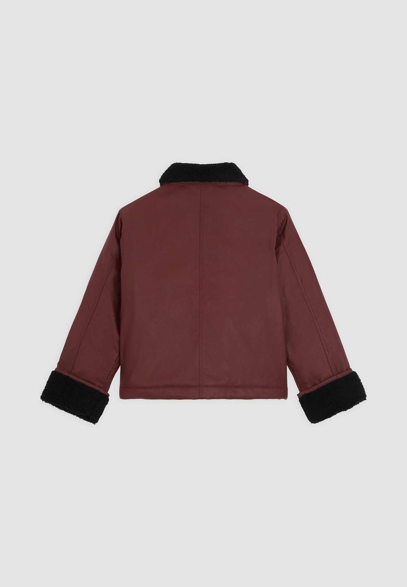 Giacca bordeaux con colletto e polsini in shearling nero. Caratterizzata da una finitura liscia e un taglio relax. La vista posteriore mostra dei dettagli delle cuciture visibili.