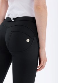 Leggings negros de cintura alta con una textura suave, presentando costuras curvas, un bolsillo trasero y un pequeño acento metálico con logotipo.