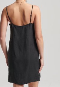 Abito nero senza maniche con spalline sottili, dalla texture liscia, lunghezza a metà coscia e un design semplice. La parte posteriore presenta un collo a goccia sottile.