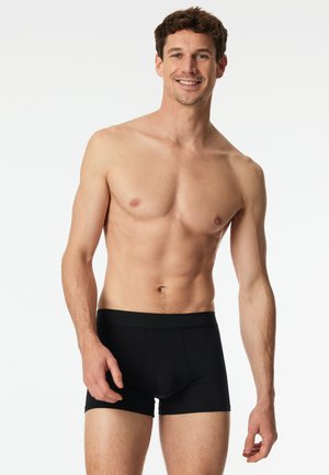 Zwarte boxershorts met een gladde tailleband, een aansluitend ontwerp en korte pijpen. De stof lijkt zacht en rekbaar. Model staat zonder shirt.