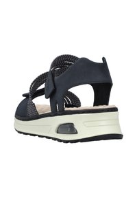 Sandale noire avec une tige en tissu texturé et des sangles Velcro, dotée d'une semelle intérieure rembourrée et d'une semelle moulée blanche avec un accent transparent.