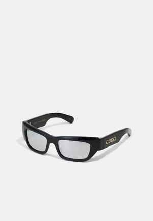 Occhiali da sole neri con finitura lucida, montatura rettangolare e lenti sfumate. Logo dorato "GUCCI" visibile sulle astine.