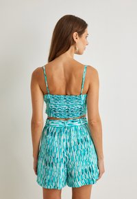 Conjunto de dos piezas que incluye un top corto de patrón azul con espalda fruncida y pantalones cortos de cintura alta en un diseño similar en turquesa.