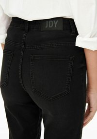 Svarta denimjeans med hög midja och två bakfickor. Har en texturerad svart etikett med "JDY" på midjebandet.