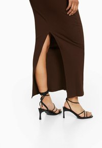 Robe maxi marron à côtes avec fentes sur les côtés, assortie à des sandales à talons noires à lanières avec un talon fin et des sangles texturées.