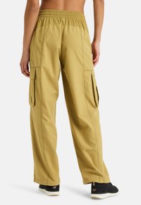 Pantaloni cargo larghi in tessuto khaki, con vita elasticizzata e tasche laterali. Texture liscia con cuciture rinforzate e senza motivi visibili.