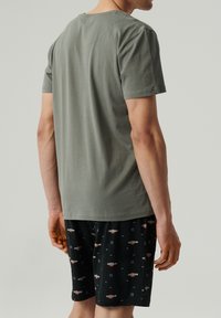 Szara bawełniana koszulka z krótkim rękawem, z okrągłym dekoltem, zestawiona z czarnymi szortami ozdobionymi małym wzorem logo.